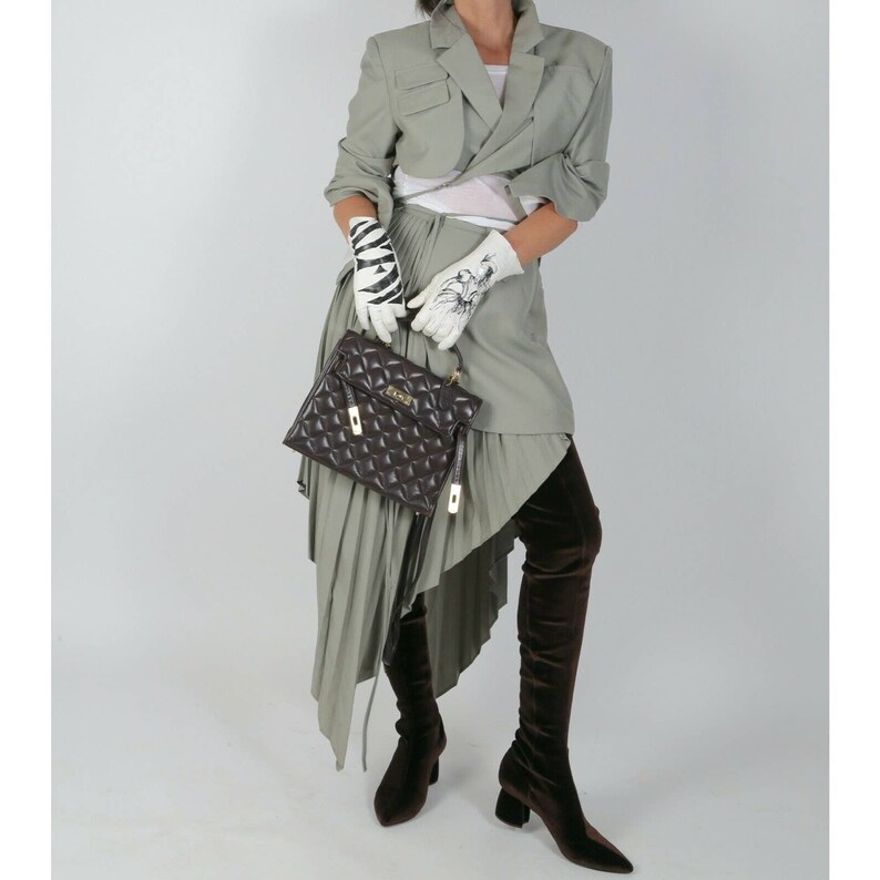 May include: A woman wearing a green cropped blazer, a white top, a green pleated skirt, and brown over-the-knee boots. She is carrying a brown quilted handbag with a gold clasp.