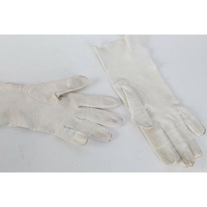 May include: A pair of white leather gloves. The gloves are laid flat on a white surface.