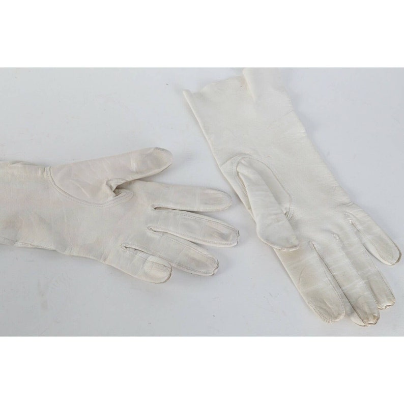 May include: A pair of white leather gloves. The gloves are laid flat on a white surface.