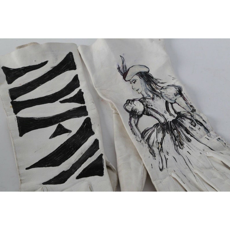 May include: A pair of white leather gloves with hand-painted designs. One glove features a black and white zebra-like pattern, while the other glove has a black and white illustration of a woman in a dress and hat.