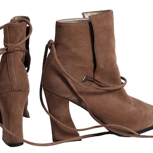 May include: A pair of brown suede ankle boots with a chunky heel and lace-up detail. The boots have a pointed toe and are tied at the ankle with long laces.