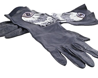 May include: A pair of dark blue leather gloves with intricate beaded embellishments. The gloves feature a design of an eye with white and black beads. The gloves are lying on a white surface.