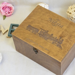 May include: A wooden box with a hinged lid and a metal latch. The box is engraved with a train, the name "Nikita", and the text "geboren am 26. Januar 2019".