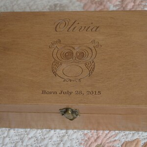 May include: A wooden box with an engraved owl and the name Olivia. The box also has the text "Born July 28, 2015".