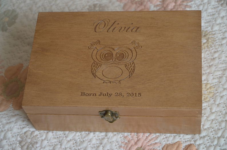 May include: A wooden box with an engraved owl and the name Olivia. The box also has the text "Born July 28, 2015".