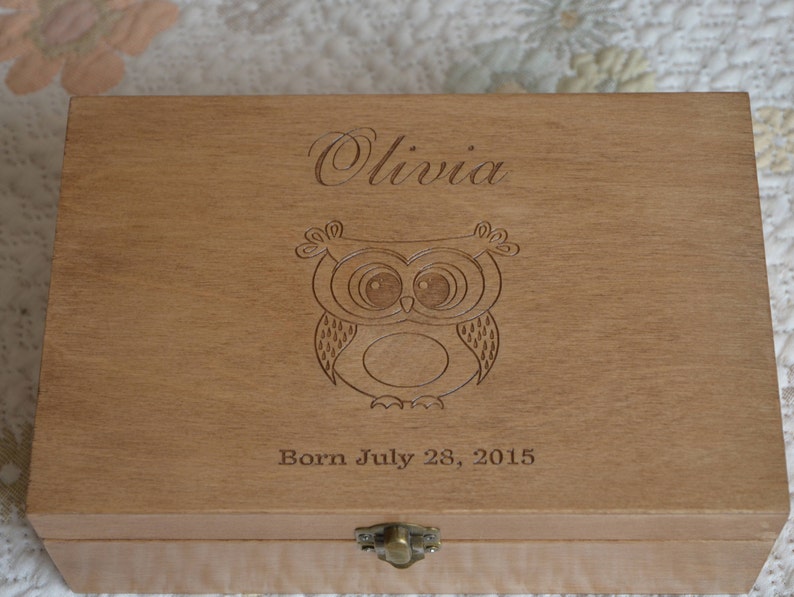 May include: A wooden keepsake box with an engraved owl design and the name "Olivia" and the date "Born July 28, 2015".