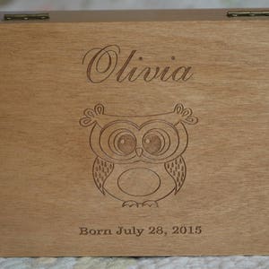 May include: Wooden keepsake box with an engraved owl and the name Olivia. The box also has the text "Born July 28, 2015".