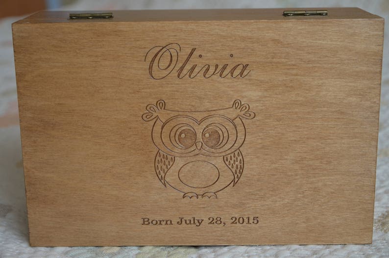 May include: Wooden keepsake box with an engraved owl and the name Olivia. The box also has the text "Born July 28, 2015".