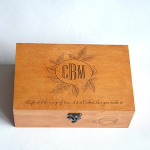May include: A wooden tea box with a hinged lid and a brass latch. The box is engraved with the initials "CBM" in a circle surrounded by leaves. The quote "Life is like a cup of tea... it's all about how you make it" is also engraved on the box.