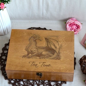 Puede incluir: Una caja de té de madera con un diseño de dragón y el texto "Tea Time" grabado en la tapa.
