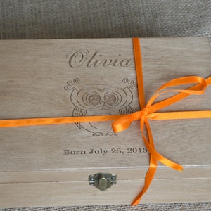Peut inclure: Une boîte en bois avec un ruban orange noué autour. La boîte est gravée du nom "Olivia" et d'un motif de hibou. Le texte "Born July 28, 2015" est également gravé sur la boîte.