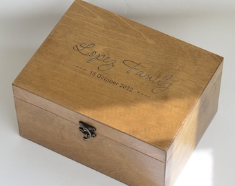 Può includere: Una scatola di legno con un coperchio incernierato e una chiusura in ottone. La scatola è incisa con il testo "Lopez Family 15 October 2022".