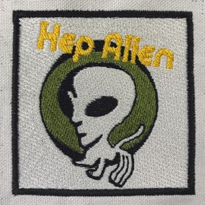 Op de afbeelding: Gestikt patch met een groene cirkel en een zwart-wit alienhoofd erin. De tekst "Neo Alien" is in geel boven de cirkel geborduurd.