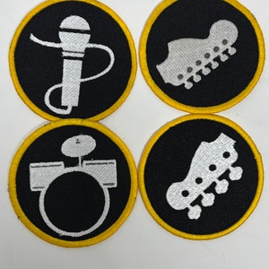 May include: Four black and white embroidered patches with yellow borders. The patches feature a microphone, a drum set, and two bass guitars.