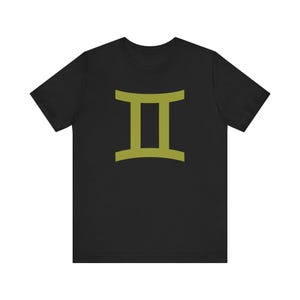 May include: Black t-shirt featuring a gold-colored Gemini zodiac symbol. The graphic is centered on the front of the shirt. The shirt has short sleeves and a crew neck.