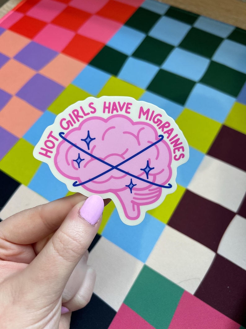 May include: A die-cut sticker featuring a pink brain illustration with two crossed dark blue lines and four small blue star icons. The text "HOT GIRLS HAVE MIGRAINES" is printed in a dark pink font along the top curve of the brain.