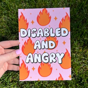 May include: A rectangular print with a light pink background featuring a repeating pattern of orange and red flames and small yellow four-pointed stars. The text "DISABLED AND ANGRY" is printed in large, bold, white letters with a thick black outline.