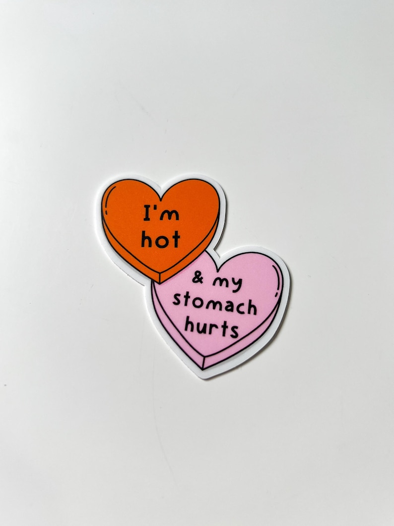 May include: Two heart-shaped stickers. The top heart is orange with the text "I'm hot" in black. The bottom heart is pink with the text "& my stomach hurts" in black. Both hearts have a white border.