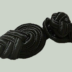 May include: Two black fabric Chinese knot toggles, also known as frog closures, with a decorative knotted design.