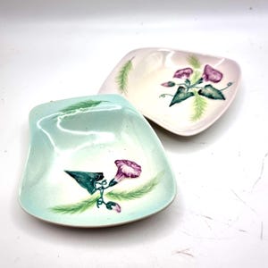 May include: Two square ceramic dishes with rounded corners, one in light mint green and one in pale pink. Each dish features a hand-painted design of purple morning glory flowers, dark green leaves, and light green feathery foliage accents.