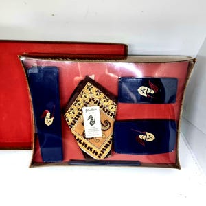 May include: A vintage gift set containing a navy blue comb, two navy blue rectangular cases, and a navy blue rectangular item. The set includes a patterned brown and gold handkerchief. Each navy blue item has a gold emblem.