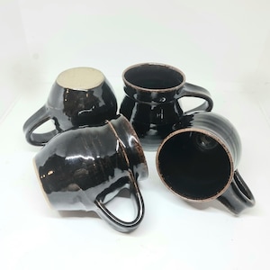 May include: Four black ceramic mugs with brown glaze. The mugs have a rounded shape and a handle on the side.