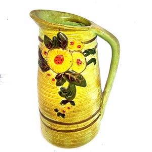 May include: A vintage ceramic jug in yellow and green. The jug is decorated with a floral pattern of yellow flowers, red centres, and green leaves. Brown horizontal stripes encircle the jug.