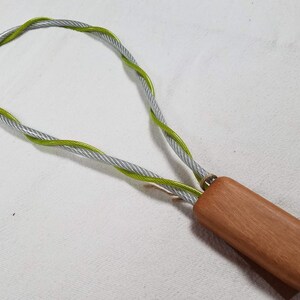 May include: A wooden handle with a silver and green braided rope attached to it. The rope is looped into a circle.