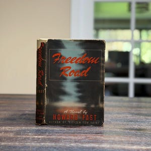 May include: A vintage copy of "Freedom Road" by Howard Fast. The book has a dark cover with the title in red script. The author's name and the title of another book are also visible. The book is slightly worn.