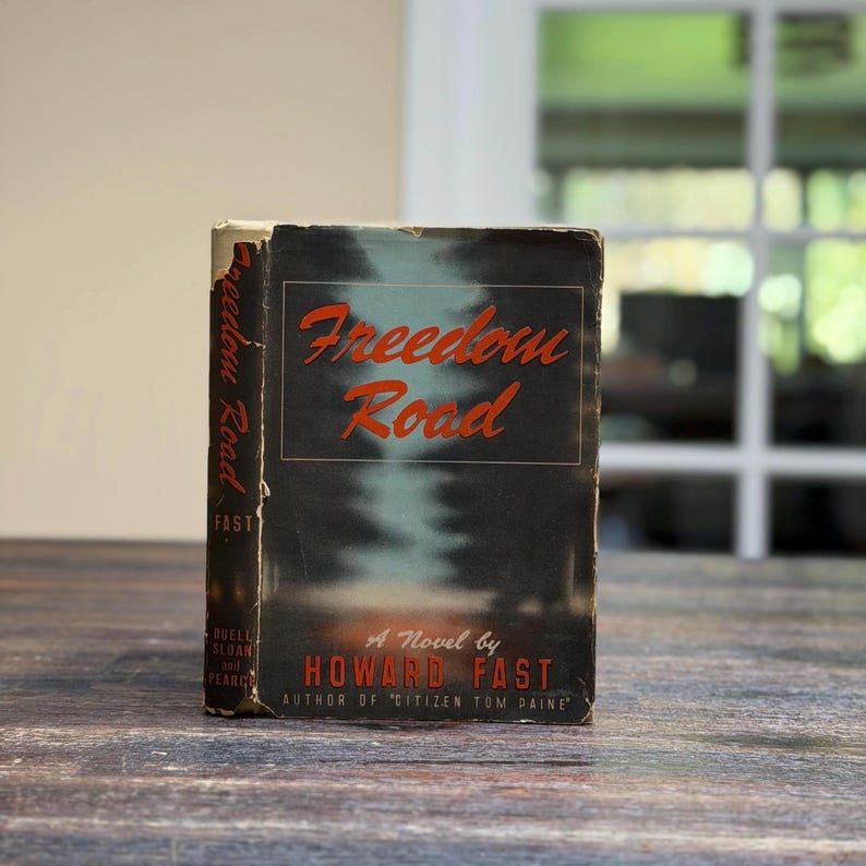 May include: A vintage copy of "Freedom Road" by Howard Fast. The book has a dark cover with the title in red script. The author's name and the title of another book are also visible. The book is slightly worn.