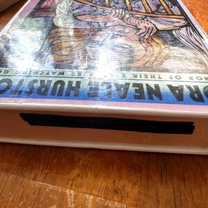 Puede incluir: Un libro con el t&iacute;tulo "ORA NEALE HURSTON" en letras azules y blancas. La portada presenta una ilustraci&oacute;n de una persona con pelo largo. El libro est&aacute; envuelto en pl&aacute;stico transparente.