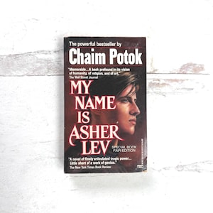 May include: A paperback book titled "My Name Is Asher Lev" by Chaim Potok. The cover features a portrait of a young man in profile, with the title in large, bold letters. The book is a special fair edition.
