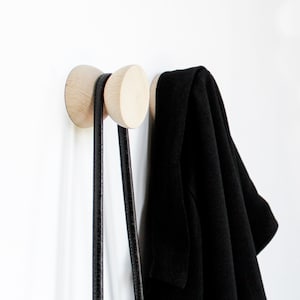 Peut inclure: Deux crochets muraux en bois avec une sangle en cuir noir suspendue.