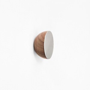 Könnte beinhalten: Ein runder Wandhaken aus Holz mit einem silbernen Metallzentrum. Der Haken ist hellbraun und hat eine glatte Oberfläche.