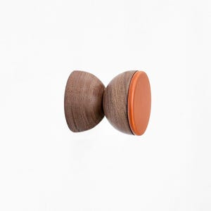 Può includere: Un gancio da parete in legno con forma arrotondata e finitura marrone. Il gancio ha un piccolo cuscinetto arancione sul fondo.