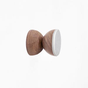 May include: A wooden wall hook with a white ceramic top. The hook is shaped like a rounded hourglass.