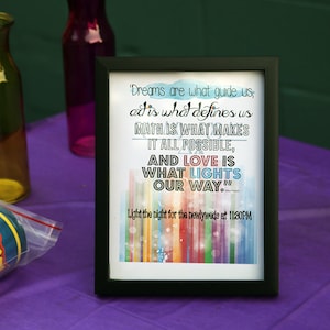 May include: A framed print with a black border featuring a quote about dreams and love. The text is in various colors against a white background with a colorful, vertical stripe design at the bottom. The print is on a purple surface.