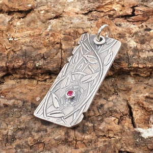 May include: A silver pendant with a detailed leafy design and a single red gemstone in the center.
