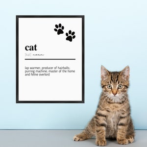 Peut inclure: Une définition imprimable en noir et blanc du mot "chat" avec un adorable chaton tabby assis devant. La définition se lit comme suit : "chauffe-jambes ; producteur de boules de poils ; machine à ronronner ; maître de la maison et seigneur félin."