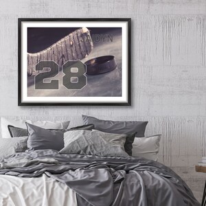 May include: A framed print of a hockey stick with the number 28 and the name Jaidyn. A ring with the words "Of Kings" is resting on the stick.