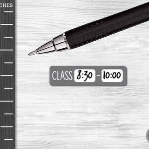May include: A gray sticker with the text "CLASS 8:30 - 10:00" on a white wooden surface. A black pen is lying on the surface.