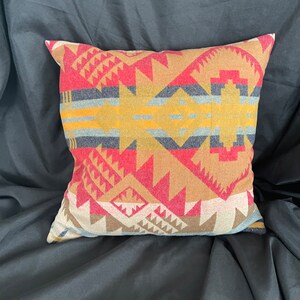 May include: A decorative throw pillow with a geometric pattern in shades of red, brown, yellow, and blue. The pillow is made of a soft, woven fabric.