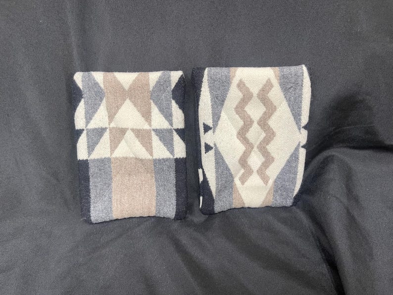 May include: Two fabric swatches with geometric patterns. One swatch has a black, white, and brown geometric pattern with triangles. The other swatch has a black, white, and brown geometric pattern with wavy lines.