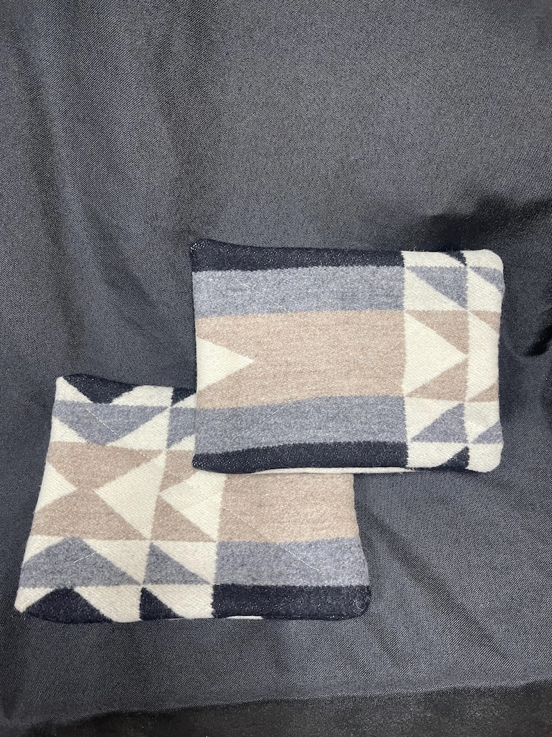 May include: Two decorative throw pillows with a geometric pattern in shades of white, beige, gray, and black. The pillows are made of a soft, woven fabric.