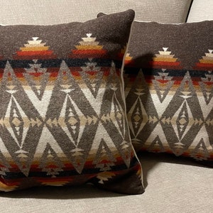May include: Two brown throw pillows with a geometric pattern in shades of brown, white, red, and orange. The pillows have a white border.