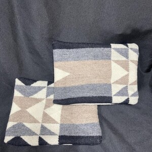 May include: Two decorative throw pillows with a geometric pattern in shades of white, beige, gray, and black. The pillows are made of a soft, woven fabric.