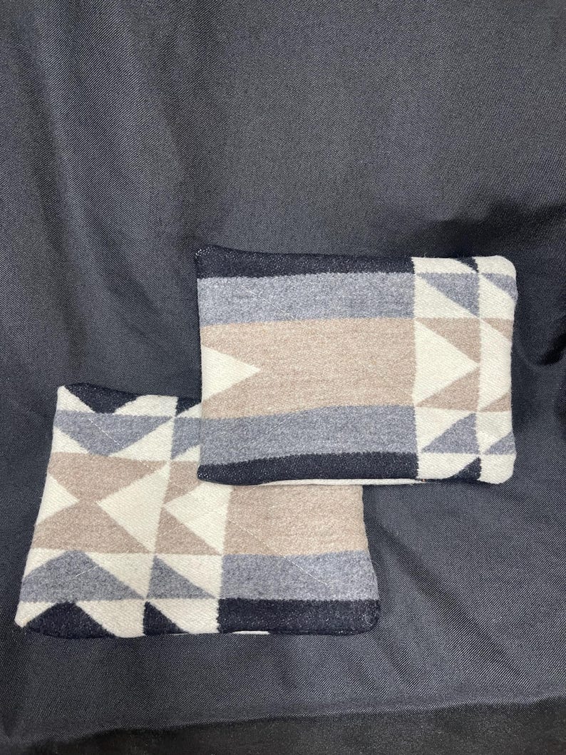 May include: Two decorative throw pillows with a geometric pattern in shades of white, beige, gray, and black. The pillows are made of a soft, woven fabric.