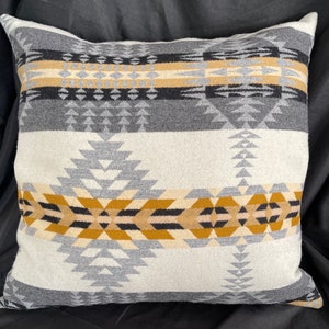 May include: A white pillow with a geometric pattern in shades of gray, black, and gold. The pattern is a repeating design of triangles and diamonds.