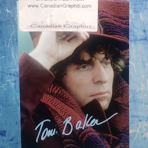 May include: A photographic print featuring a portrait of Tom Baker wearing a dark hat and a thick, multi-colored knit scarf. The image includes a white sticker at the top with the text DO NOT COPY ORIGINAL ITEM FROM www.CanadianGraphiti.com.