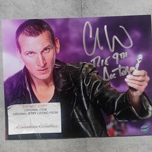 May include: A rectangular photograph featuring a person in a black leather jacket against a purple background, holding a sonic screwdriver. The image includes a silver signature, the text "The 9th Doctor," and a "DO NOT COPY" label.